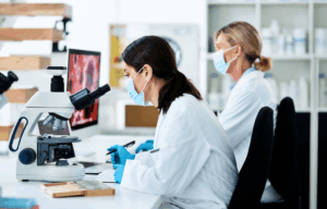 Dwóch pracowników laboratorium analizujących próbki pod mikroskopem w czasie pracy.